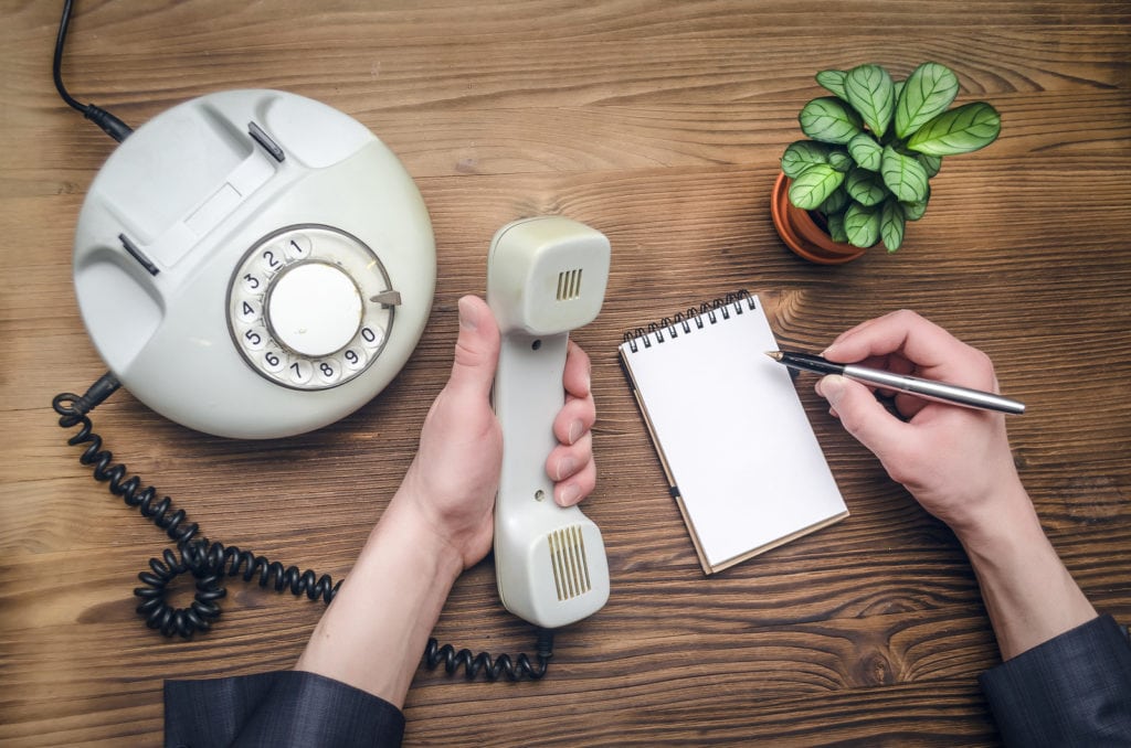 Telephone in male businessman hands and notebook with copy space on office table. Contact us. Business conversation.